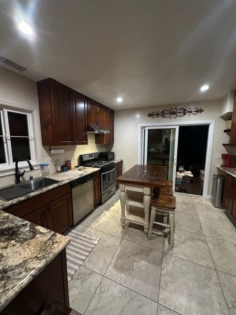 Modern kitchen with wood cabinets, granite countertops, and a dining table by the sliding door.