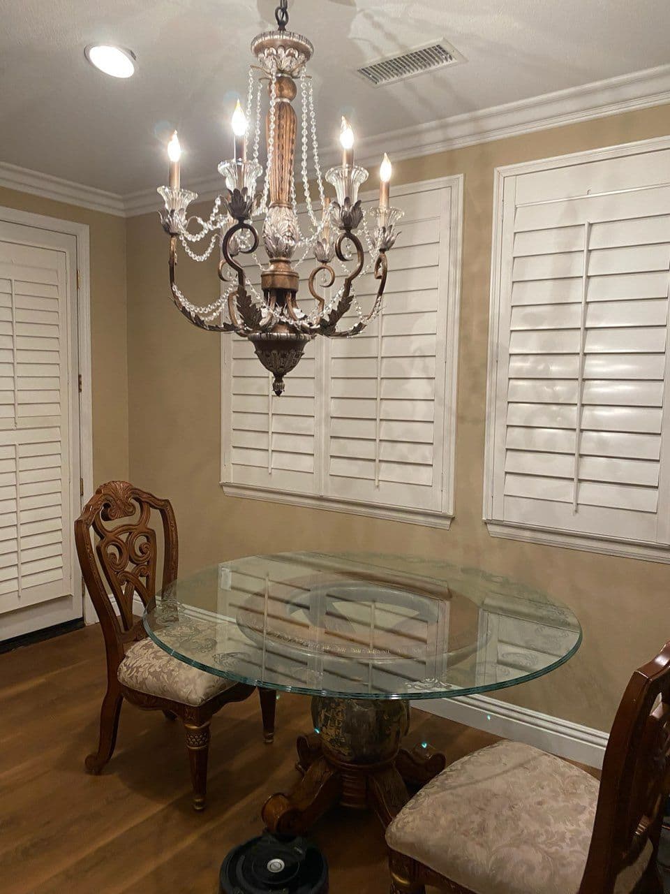 Elegant dining area with a glass table, antique chairs, and a crystal chandelier.